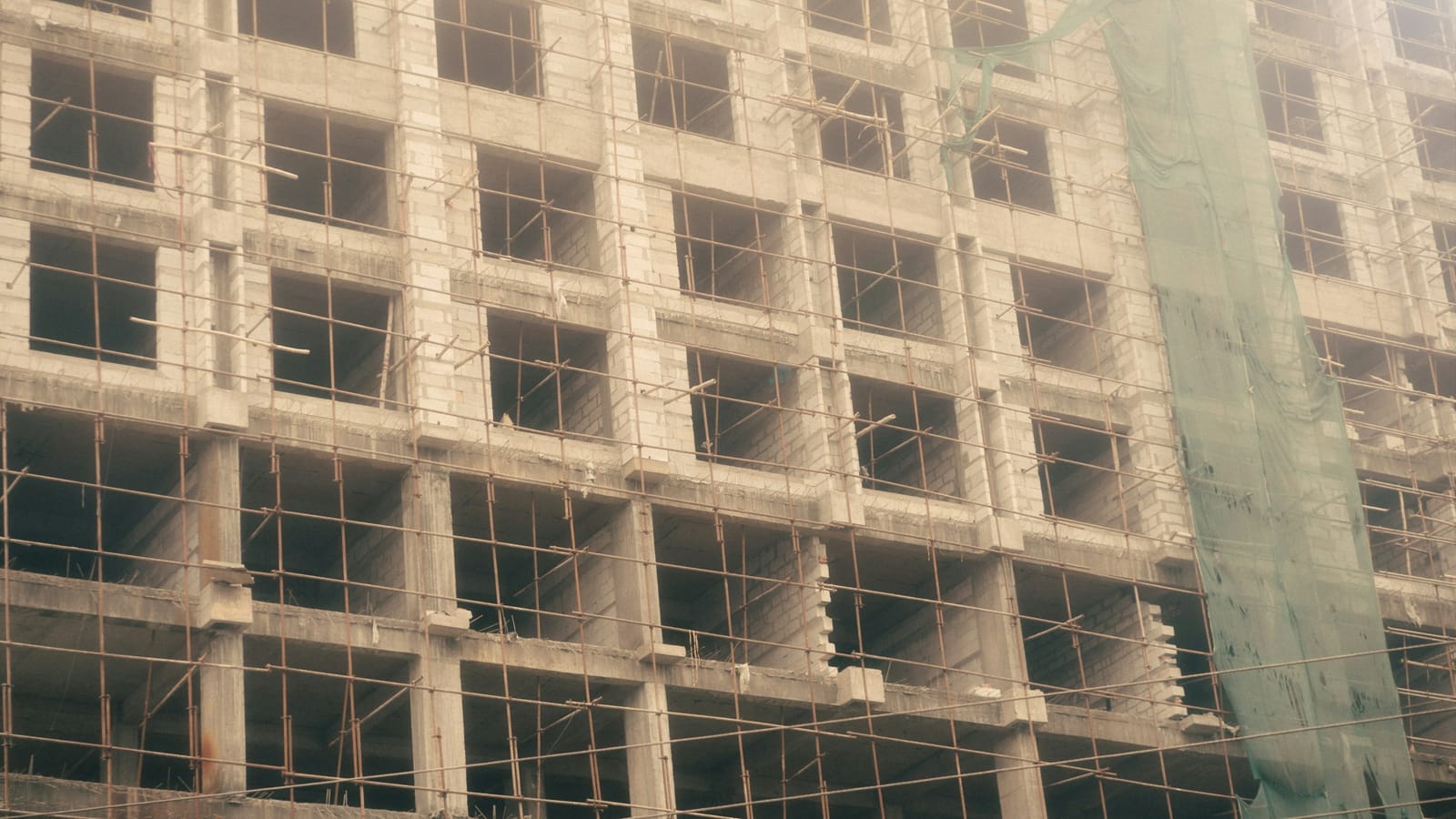 Pencere boşlukları ve iskele boruları görünen, yapımı süren betonarme bir apartman cephesi