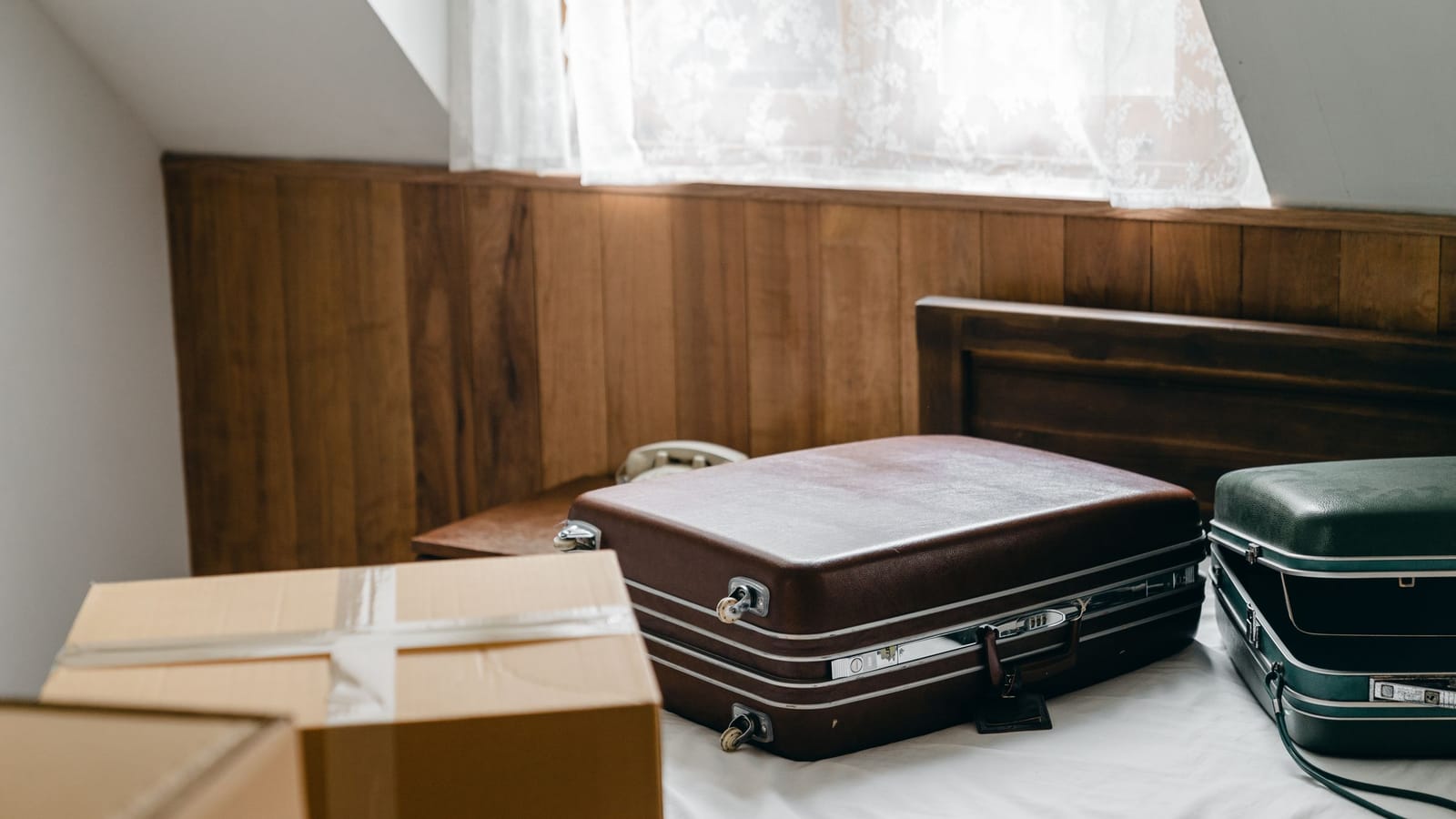 Two vintage suitcases and packed moving boxes in a room by a curtained window