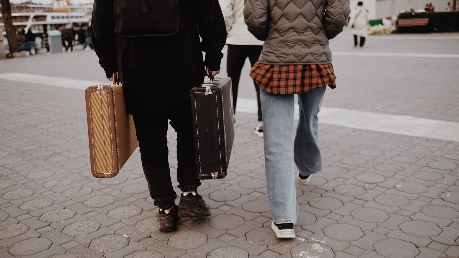 Two travellers carrying suitcases along a paved street