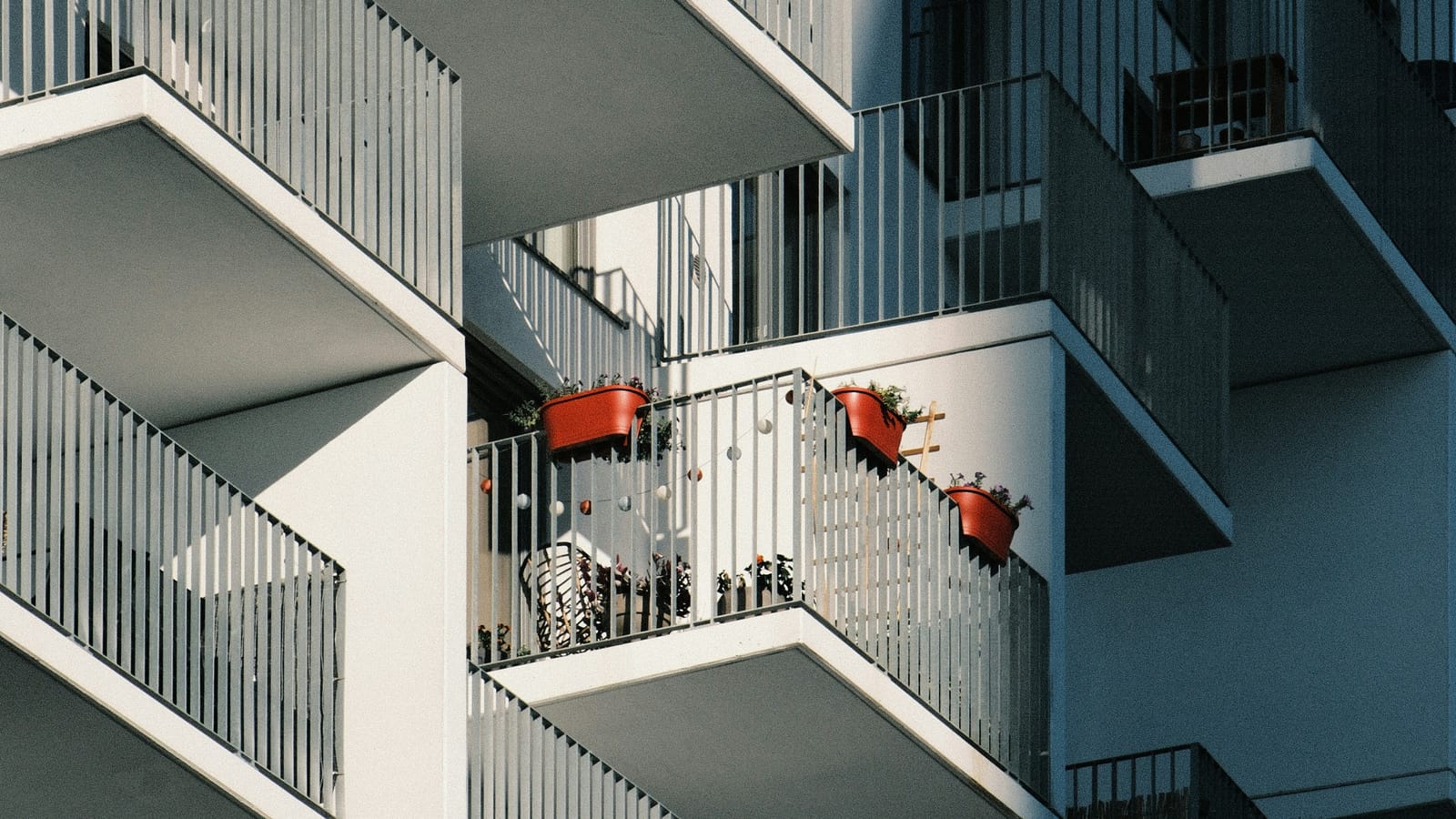 Apartman cephesinde üst üste sıralanan beyaz balkonlar ve saksılı bir balkon