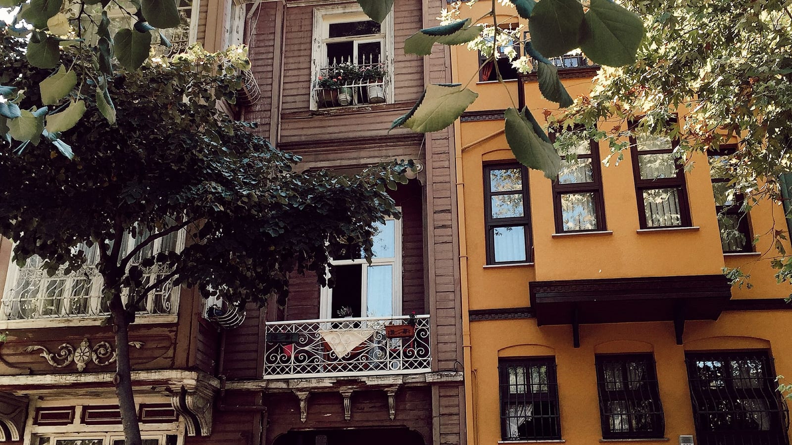 Kuzguncuk'ta ağaçların arasından ahşap ve sarı cepheli eski konutlar